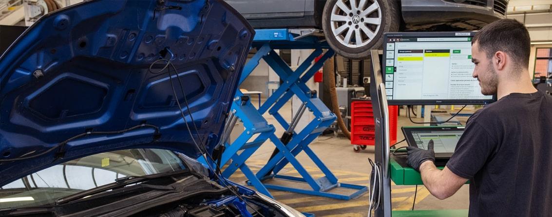 Apprenti manipulant une console branchée sur une voiture dont le capot est ouvert