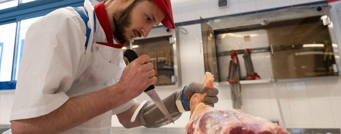 Apprenti boucher travaillant au couteau sur un morceau de viande