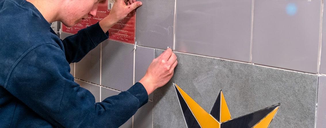 Apprenti en train de poser des croisillons entre des dalles de carrelage