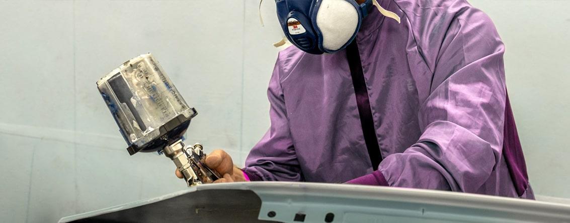 Peintre automobile en tenu avec un masque et un pistolet en train de peindre une portière