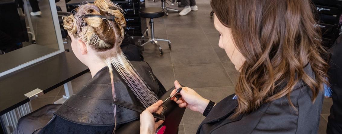 Apprenti coiffeuse mesurant une mèche de cheveux avec ses doigts ciseaux à la main