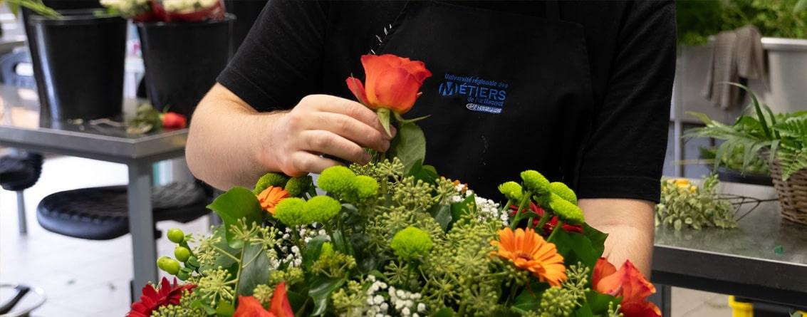 Jeune apprentie fleuriste apporte la touche finale à la conception d'un bouquet en ajoutant une rose orange