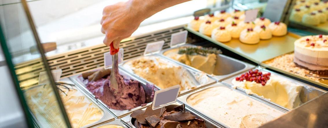Bacs de glace au multiple parfums. Une main prépare une glace avec un portionneur