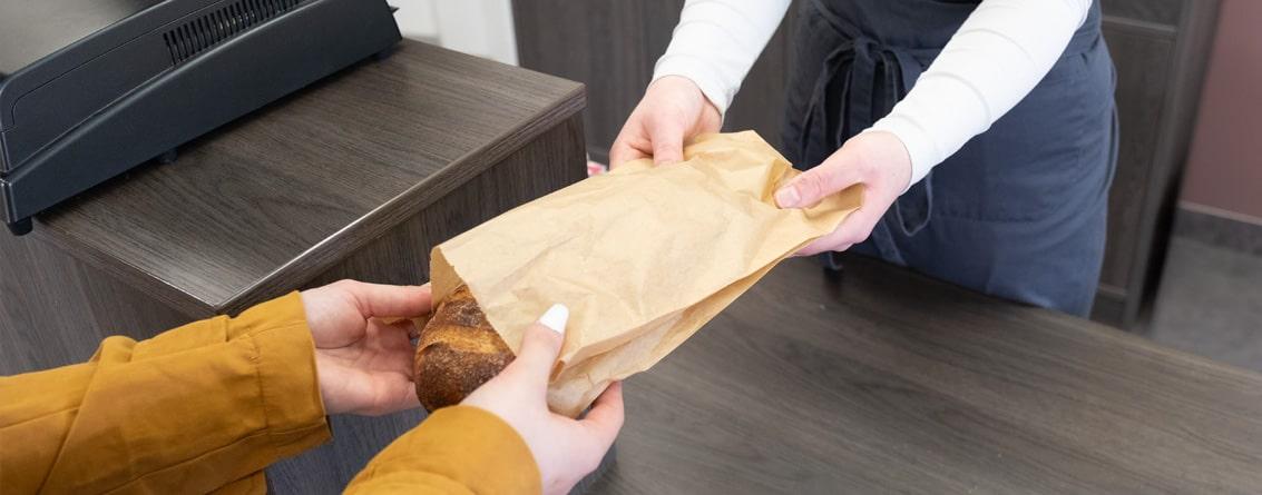 Un boulanger tend un pain dans un emballage Craft à un client