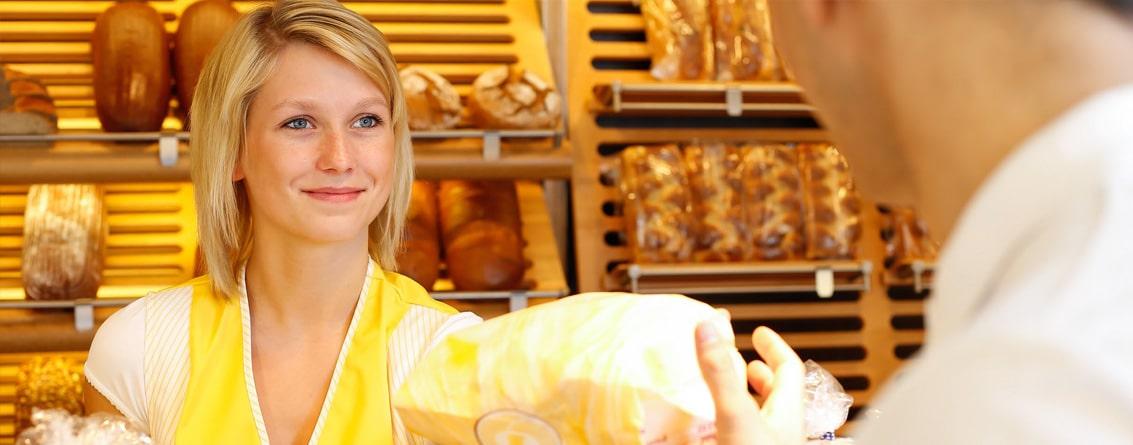 Une jeune boulangère tend un produit à un client