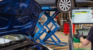 Apprenti manipulant une console branchée sur une voiture dont le capot est ouvert