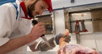 Apprenti boucher travaillant au couteau sur un morceau de viande