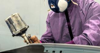 Peintre automobile en tenu avec un masque et un pistolet en train de peindre une portière