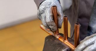 Mains gantés qui tiennent un montage de tuyaux en cuivre dans un étau