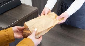 Un boulanger tend un pain dans un emballage Craft à un client